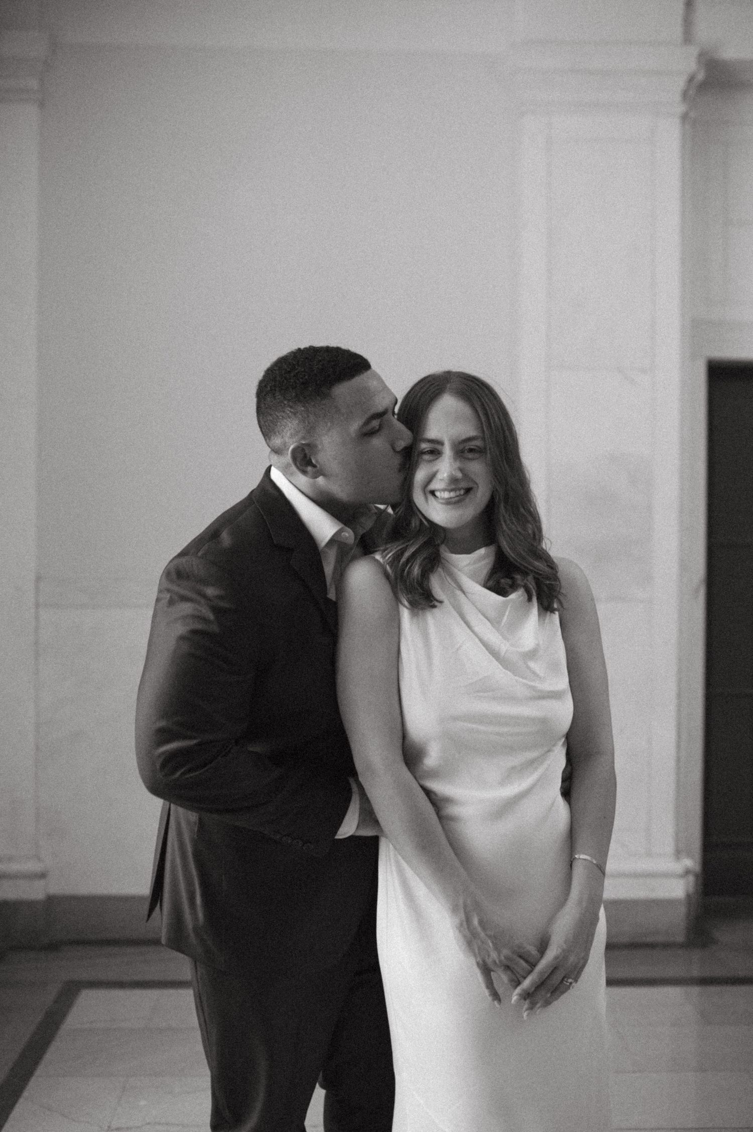 A playful black and white portrait showing affection between a couple in formal wear.