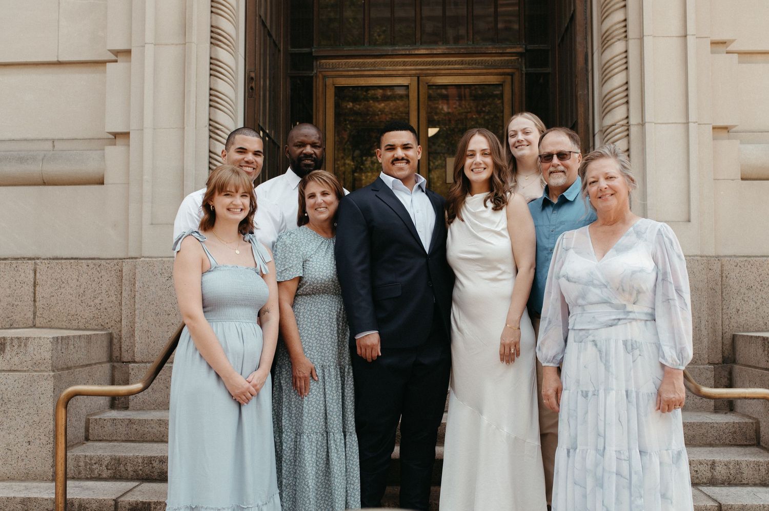 Wedding party posed on stone steps wearing coordinated blue and white formal attire.