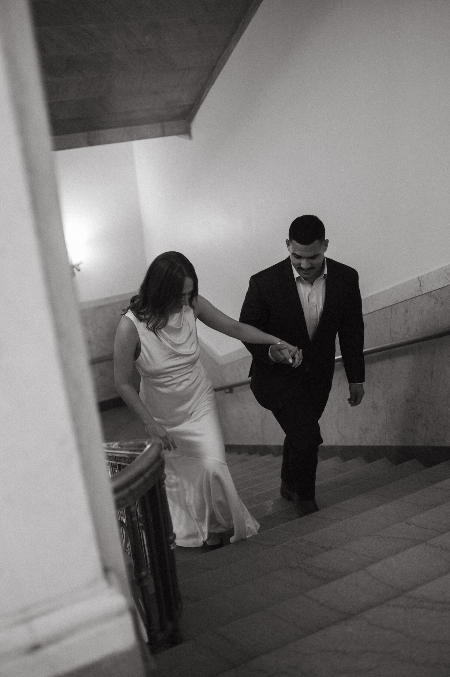 A couple ascending stairs together in formal wear, holding hands.