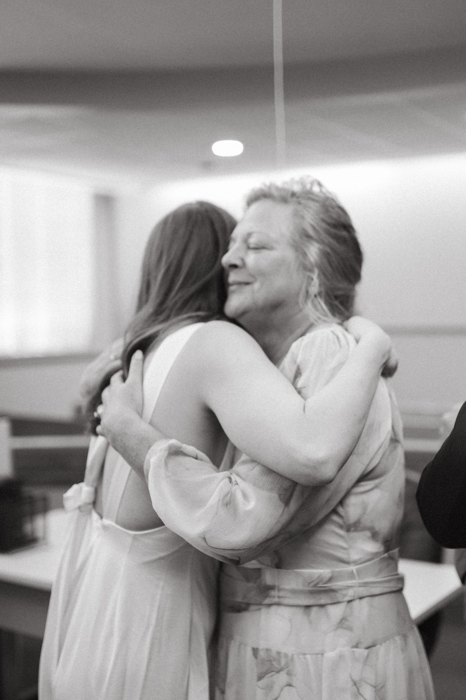 An emotional embrace shared between two women in formal attire at an indoor event.