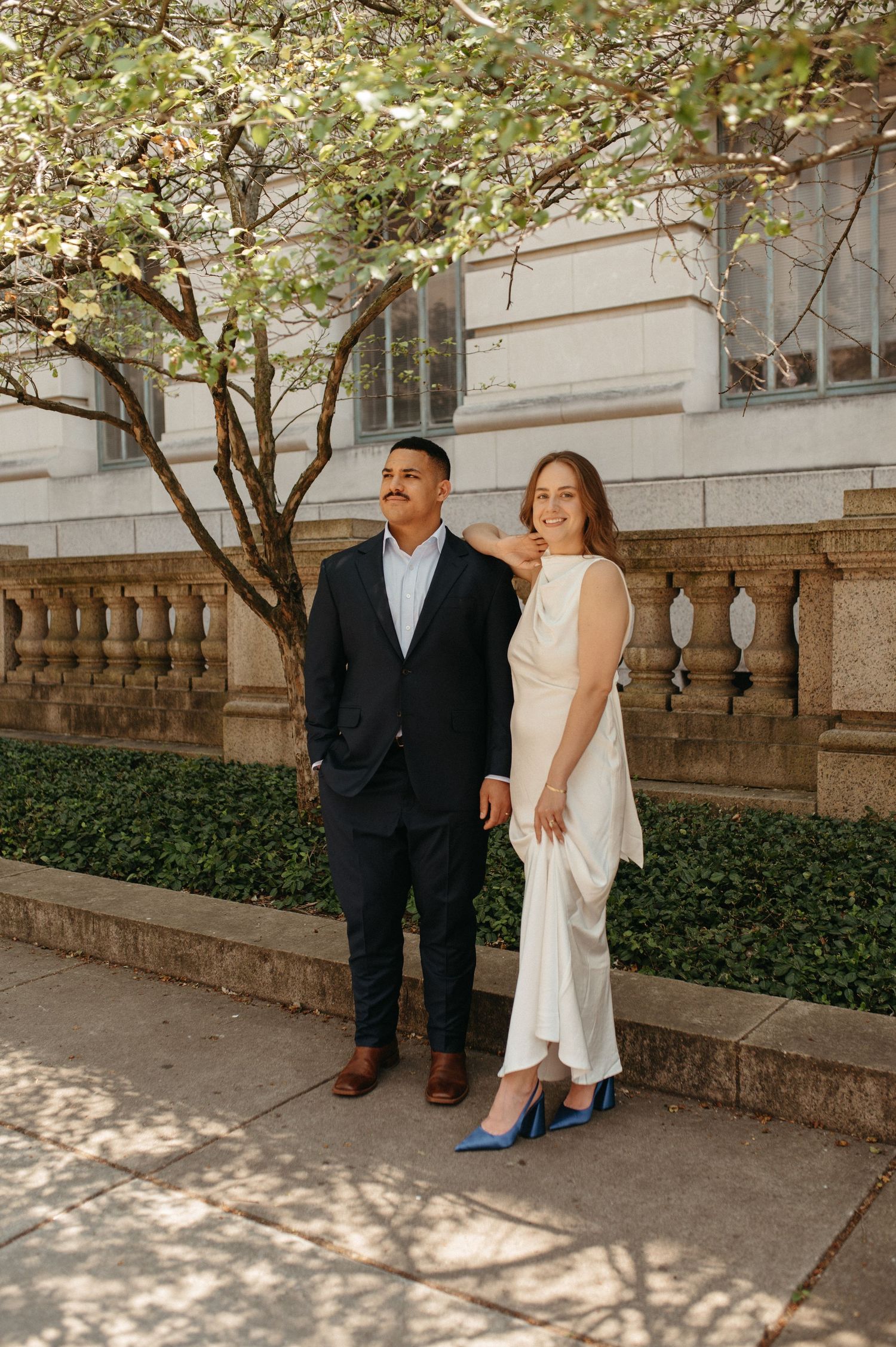 Elegant couple in formal attire poses together outside historic building.