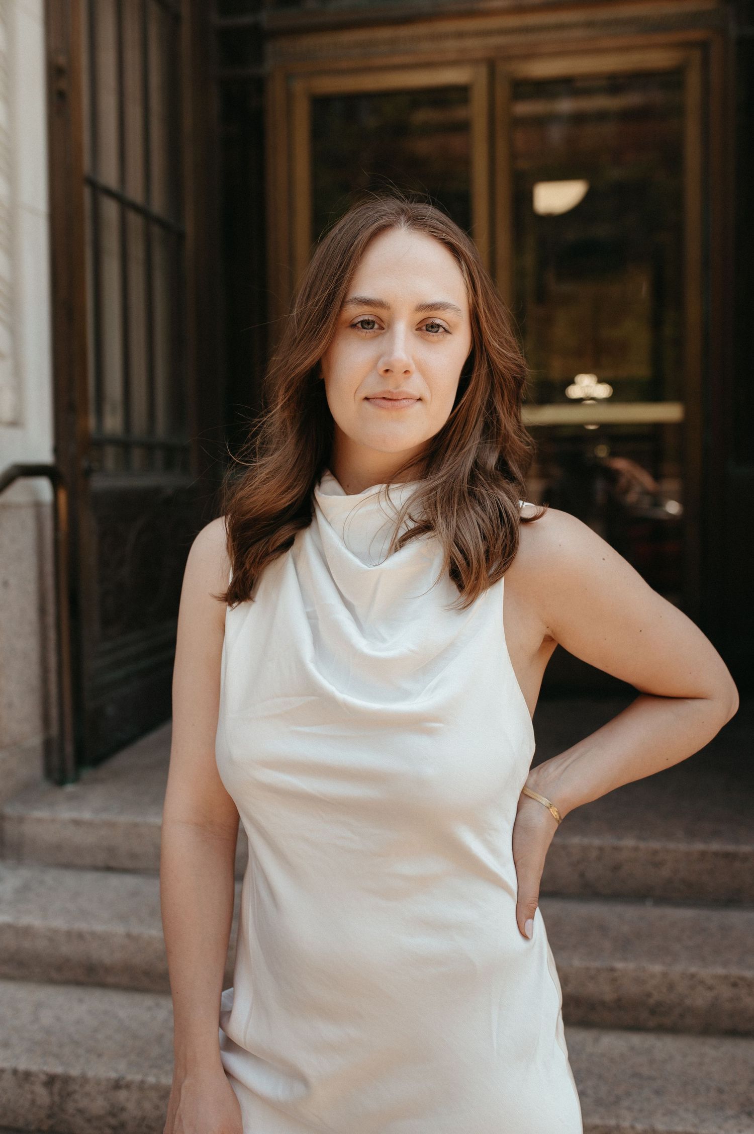 Woman in elegant white sleeveless dress poses on stone steps near classic architecture.