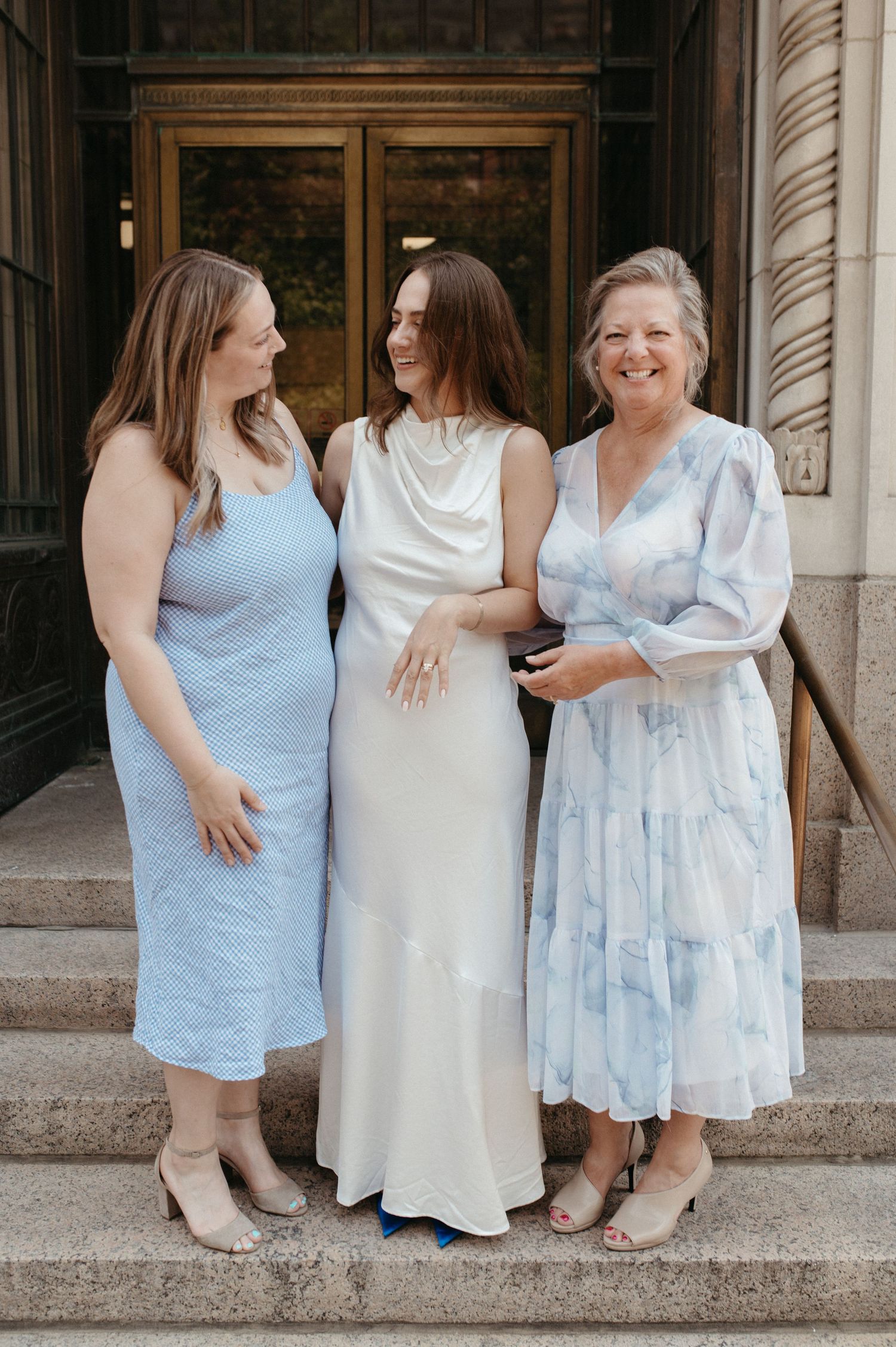 Three women in coordinating blue and white dresses standing together on stone steps.