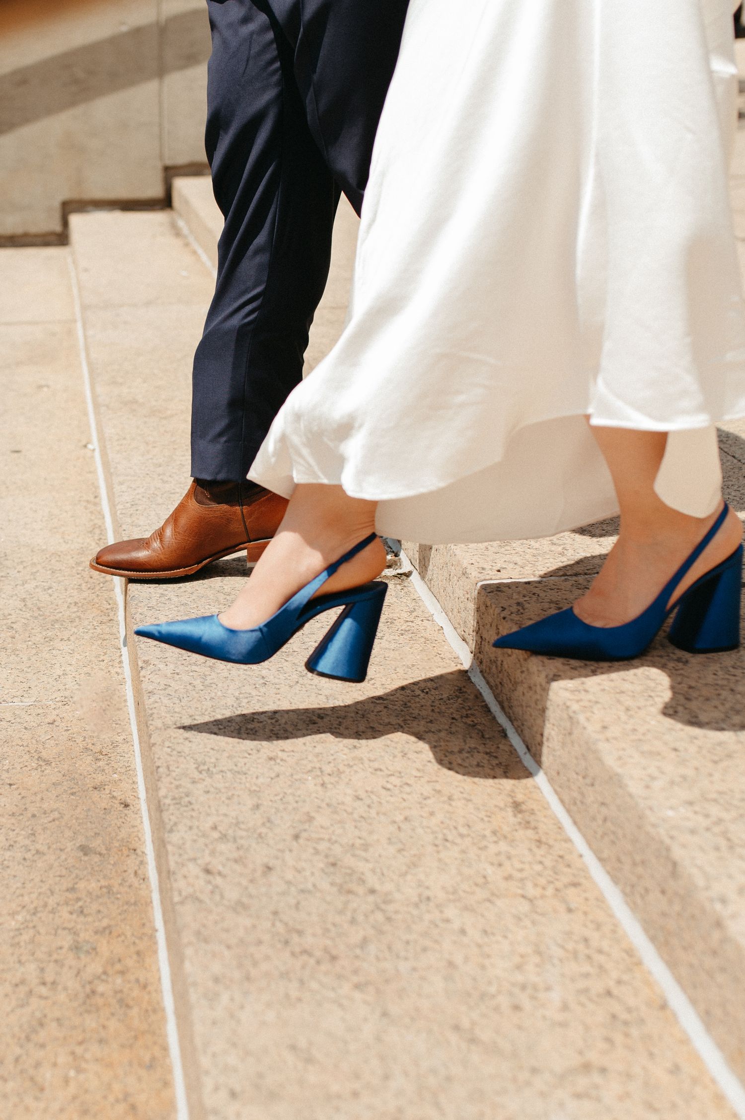 Detail shot of blue heels and brown dress shoes on stone steps during wedding photoshoot.