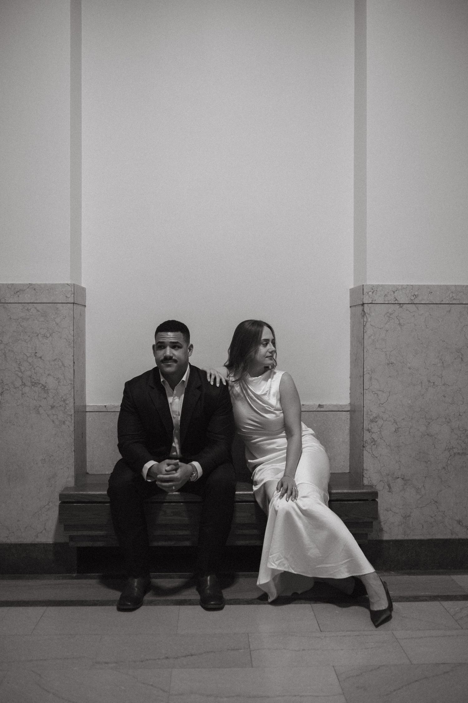 Black and white portrait of couple seated on bench in formal attire.