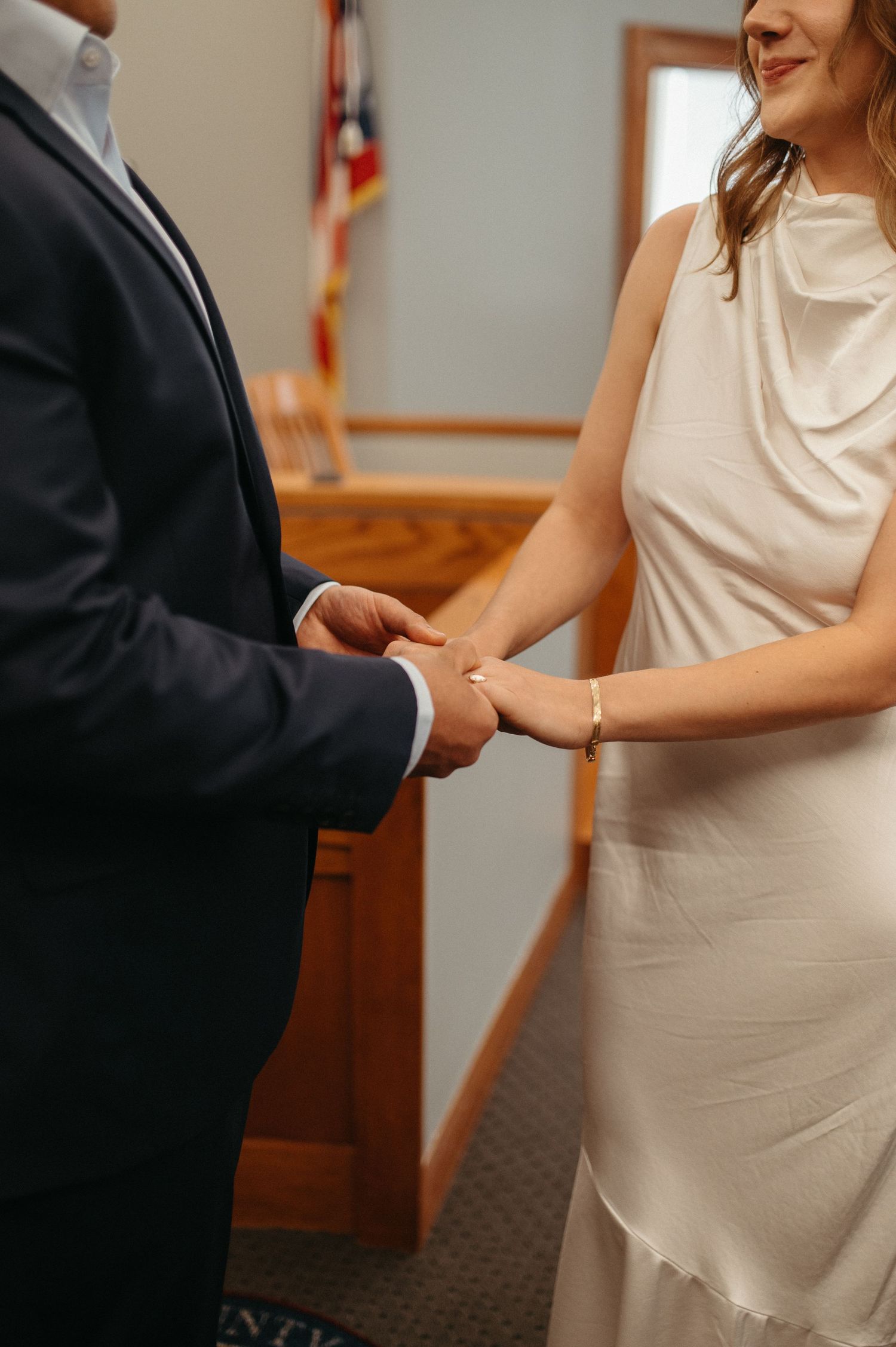 Close-up of couple holding hands during courthouse ceremony.