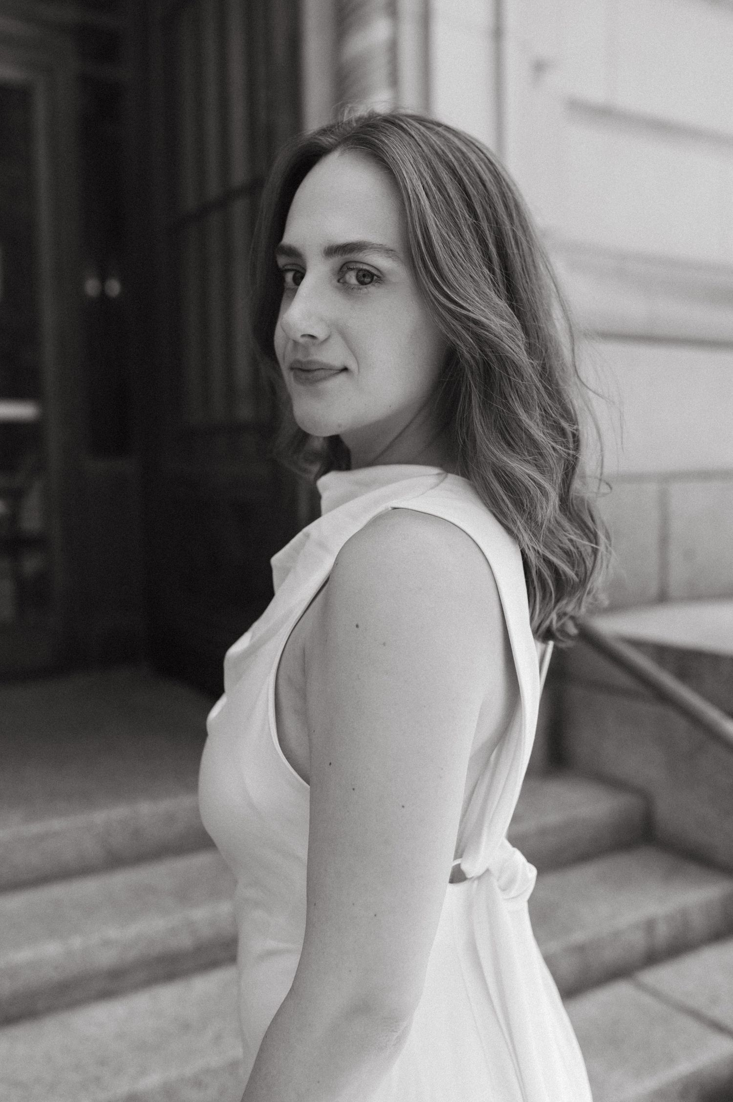 Woman in sleeveless white dress poses elegantly on stone steps.
