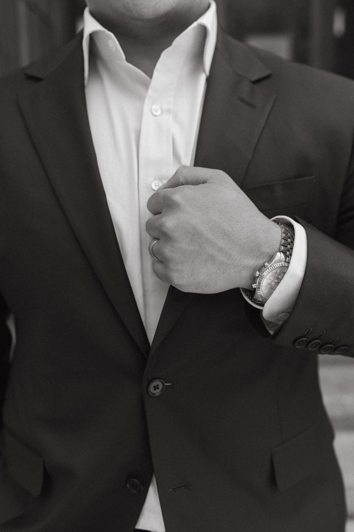 Professional man in dark suit and white shirt adjusts his lapel while wearing a watch.