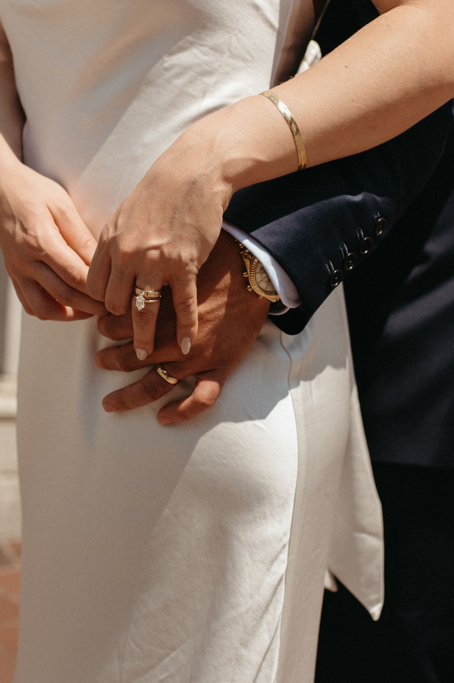 Close-up of hands with wedding rings and jewelry against formal attire.
