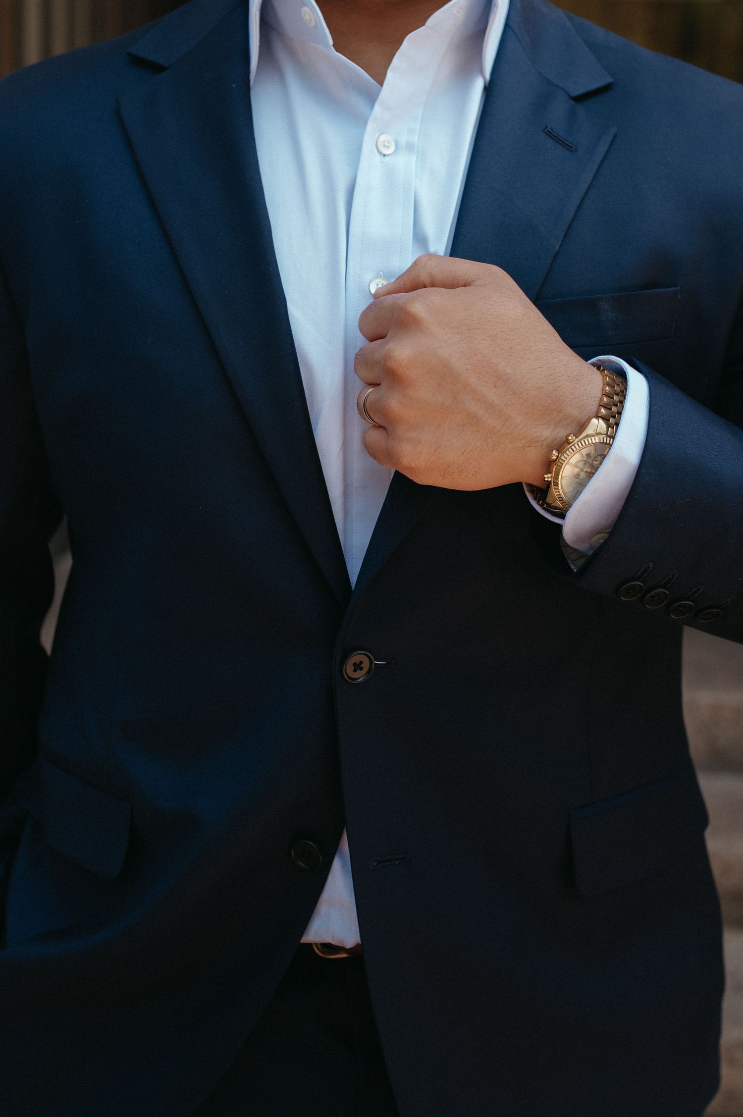 Close-up detail of navy suit jacket, white shirt, and gold watch on wrist.