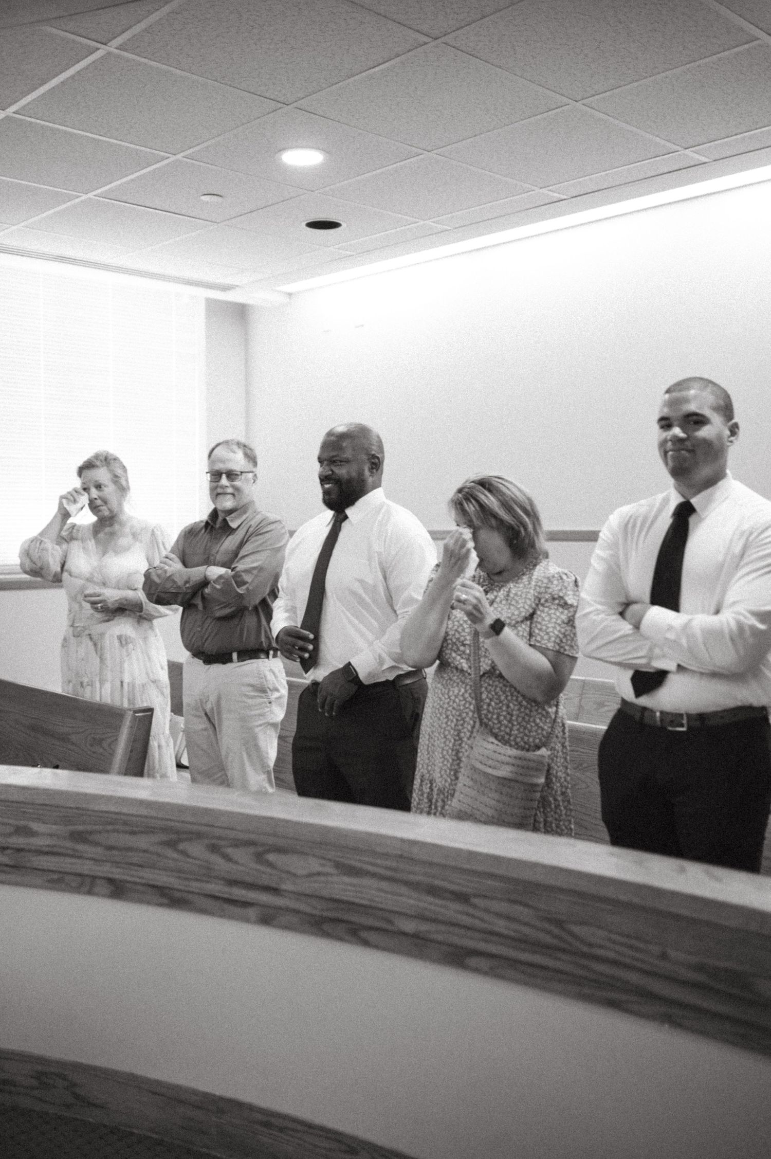 A group of wedding guests stand together sharing emotional reactions during a ceremony.