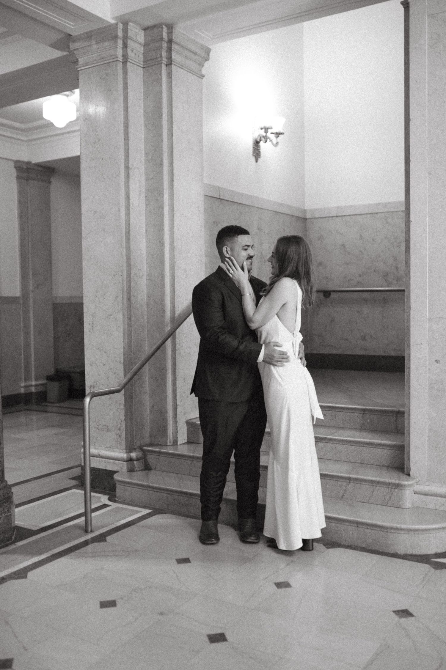 A couple in formal attire sharing an intimate moment on marble steps indoors.