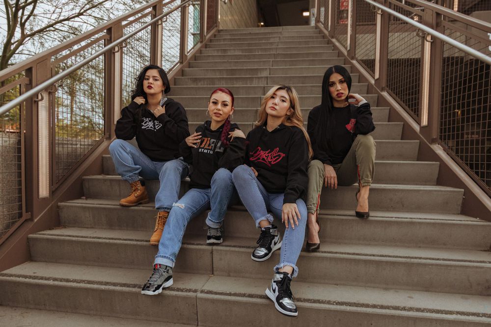 Group wearing matching black hoodies sits casually on concrete steps outdoors.