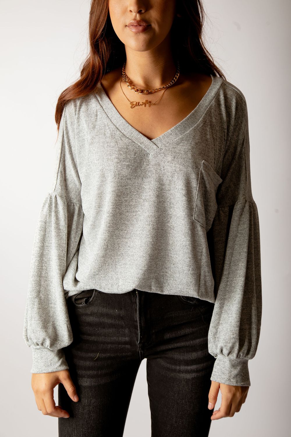 Grey v-neck sweater with balloon sleeves styled with dark jeans and gold necklace.