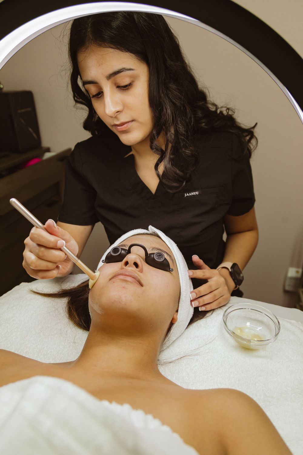Professional esthetician applies facial treatment while client wears protective eyewear.