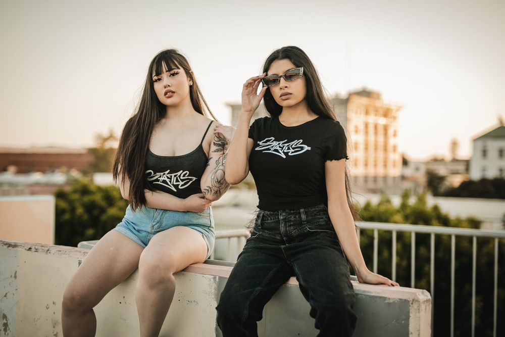 Urban lifestyle portrait of two friends in matching branded shirts on city rooftop.