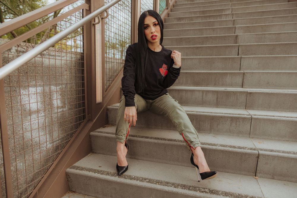Model in black sweater with red detail poses on concrete steps with railing.