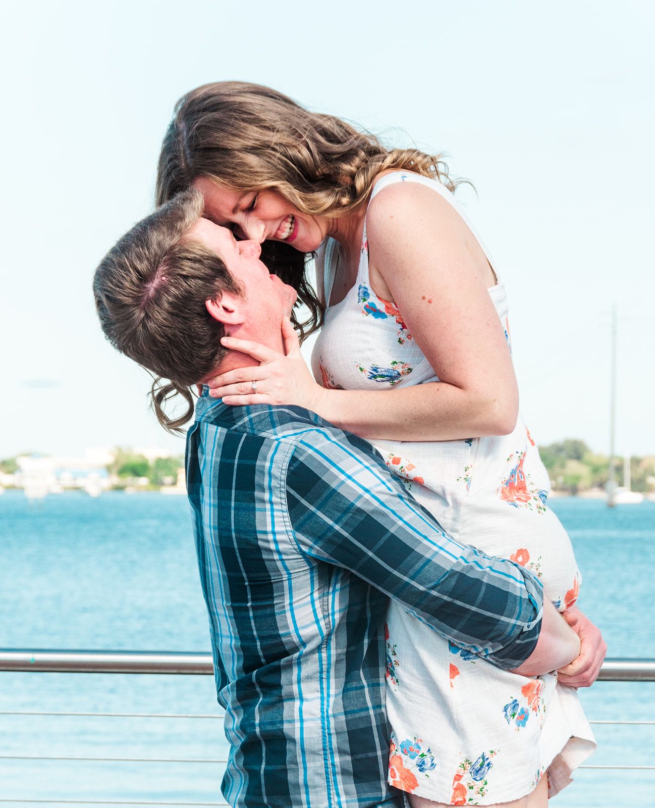 Romantic couple embracing on pier with blue water in background.