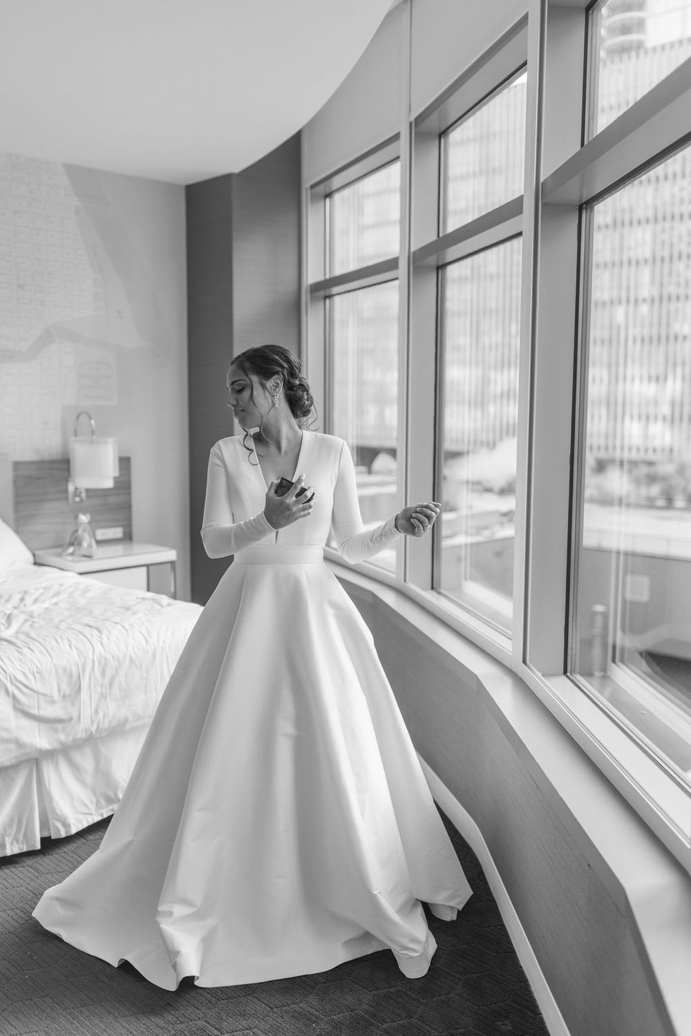 Black and white photo of bride in full ball gown looking out floor-to-ceiling windows.
