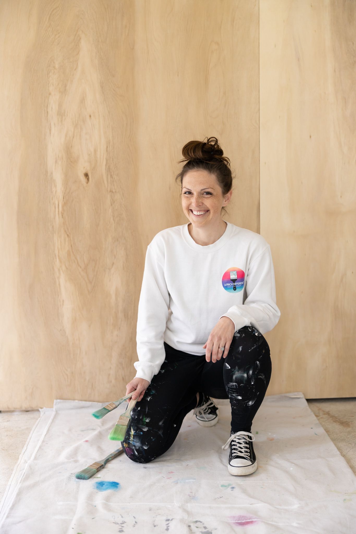 woman painter of a Pinch Different in North Bend, WA headshot in painting cloths holding paint brushes