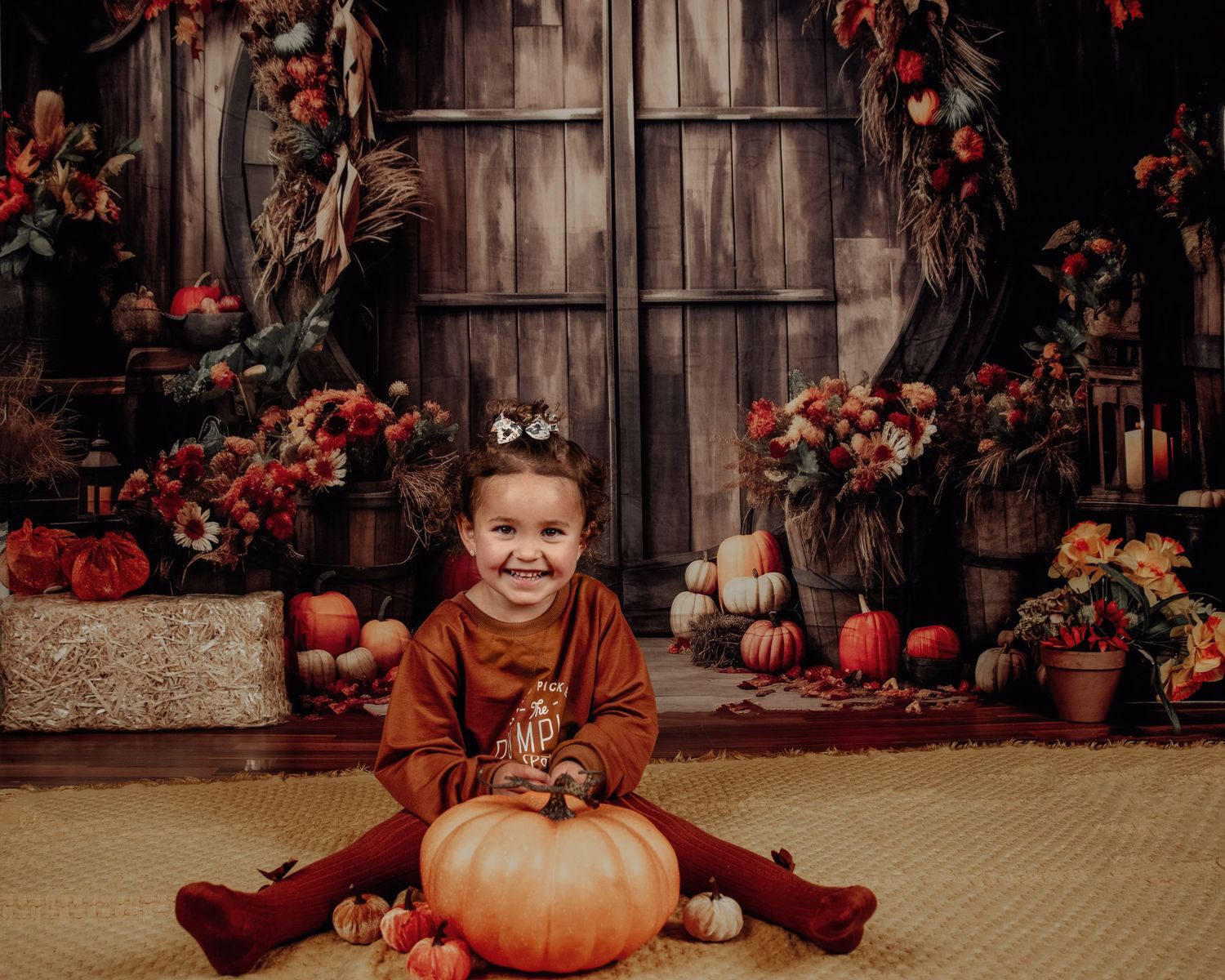 Autumn harvest scene with rustic wooden backdrop decorated with pumpkins and fall foliage.