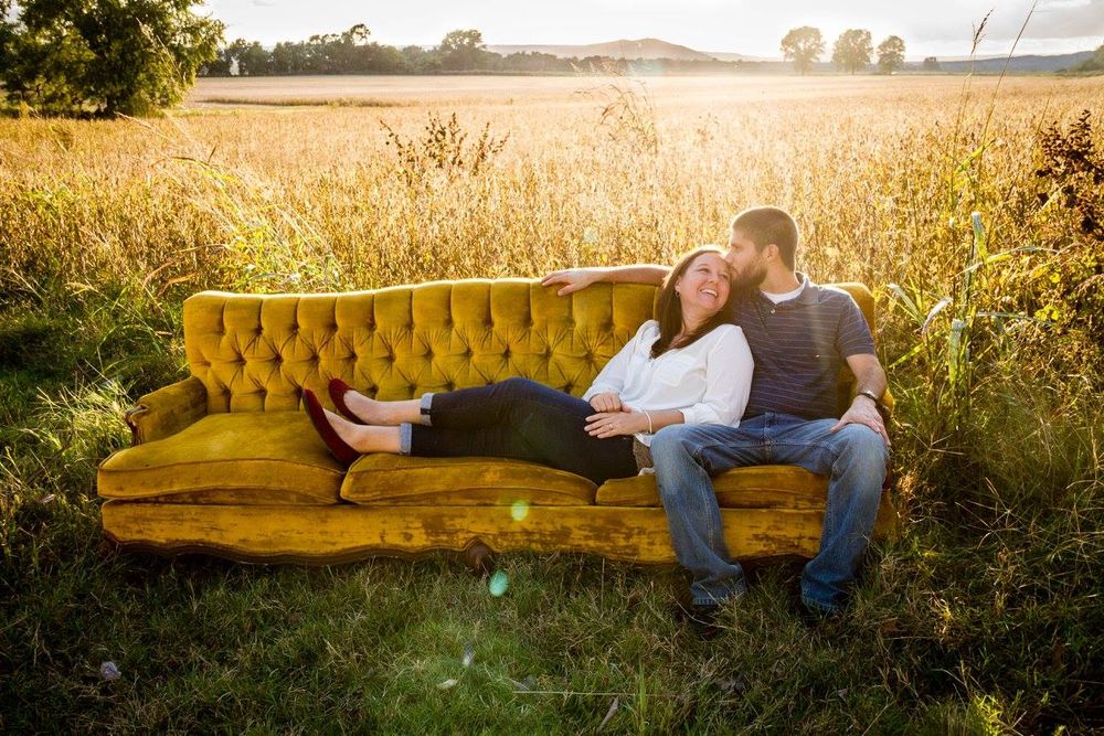 couple sitting on gold couch in a golden field in evening sunlight in Bethesda, Arkansas with girl leaned on guy and him kissing her head