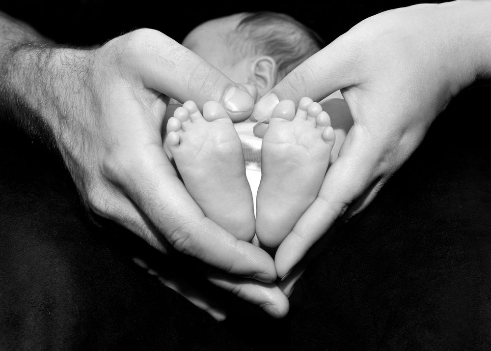 black and white photo of parent hands and baby feet