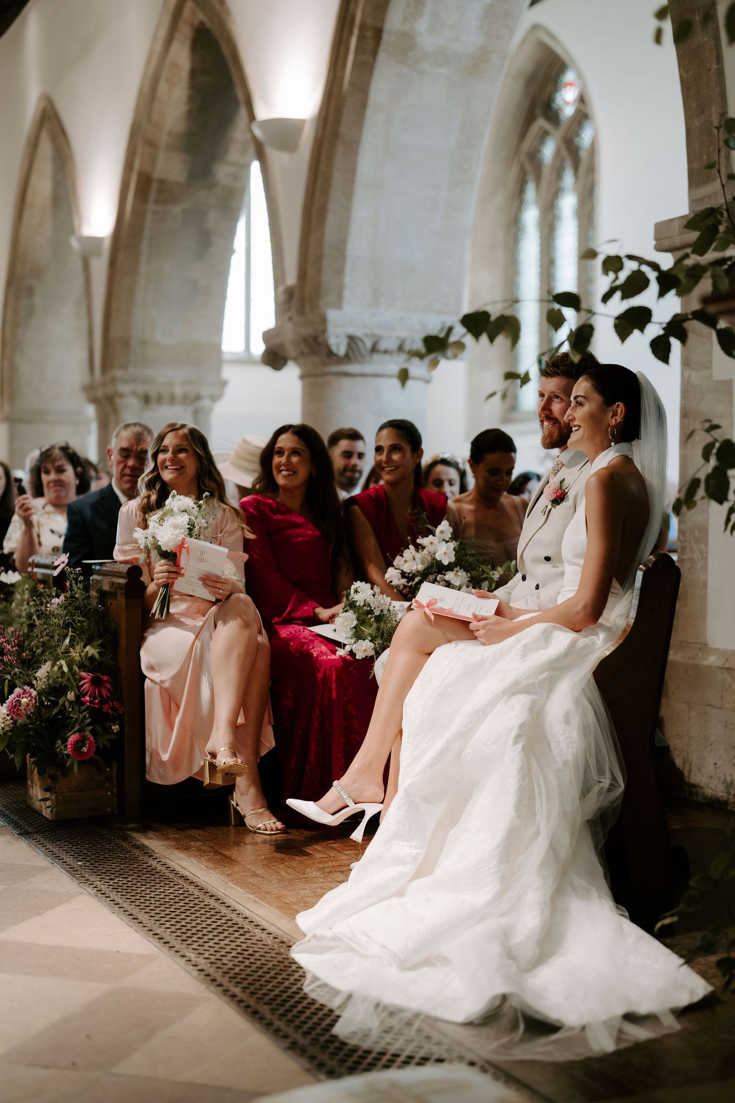 bride and groom sat smiling at the church alter during a reading at st Nicholas church in Oxfordshire