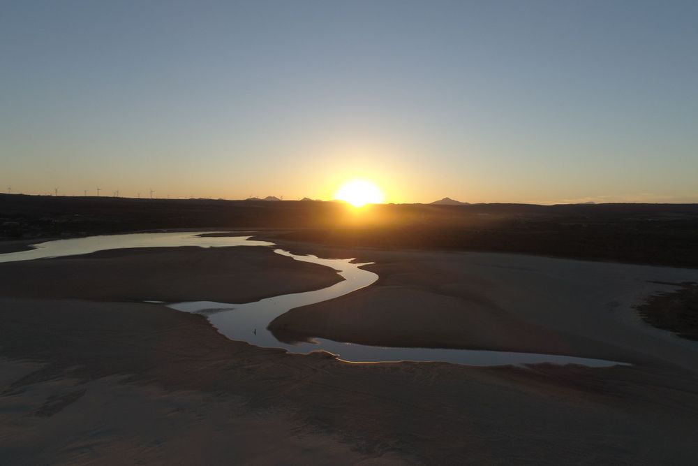 Aerial sunset view over a winding river through a vast desert landscape.