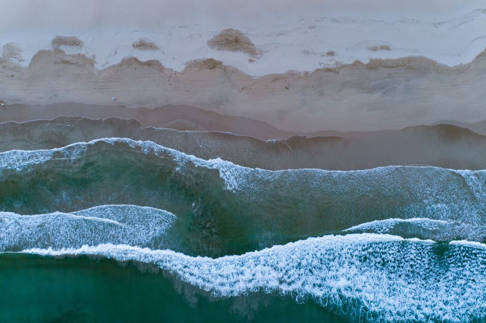 Aerial top-down view of turquoise ocean waves breaking on a sandy shore.