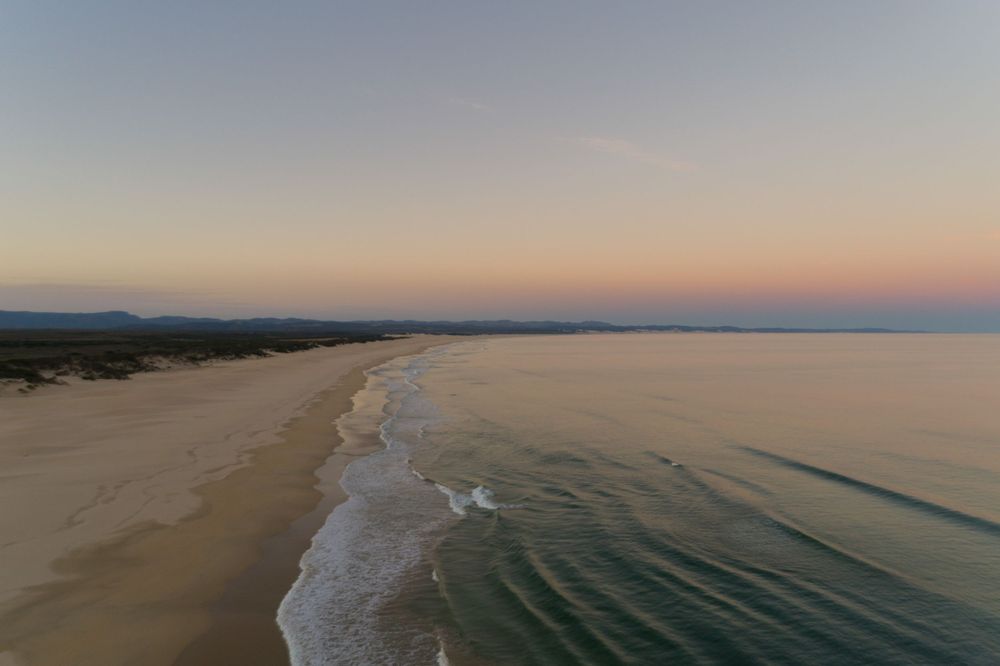 Aerial view of a long sandy beach at dusk with gentle ocean waves.