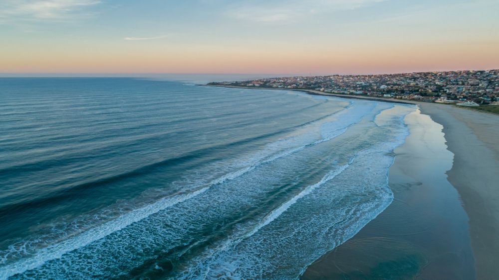 Aerial view of a serene beach at sunset with gentle waves and a coastal town in the background.