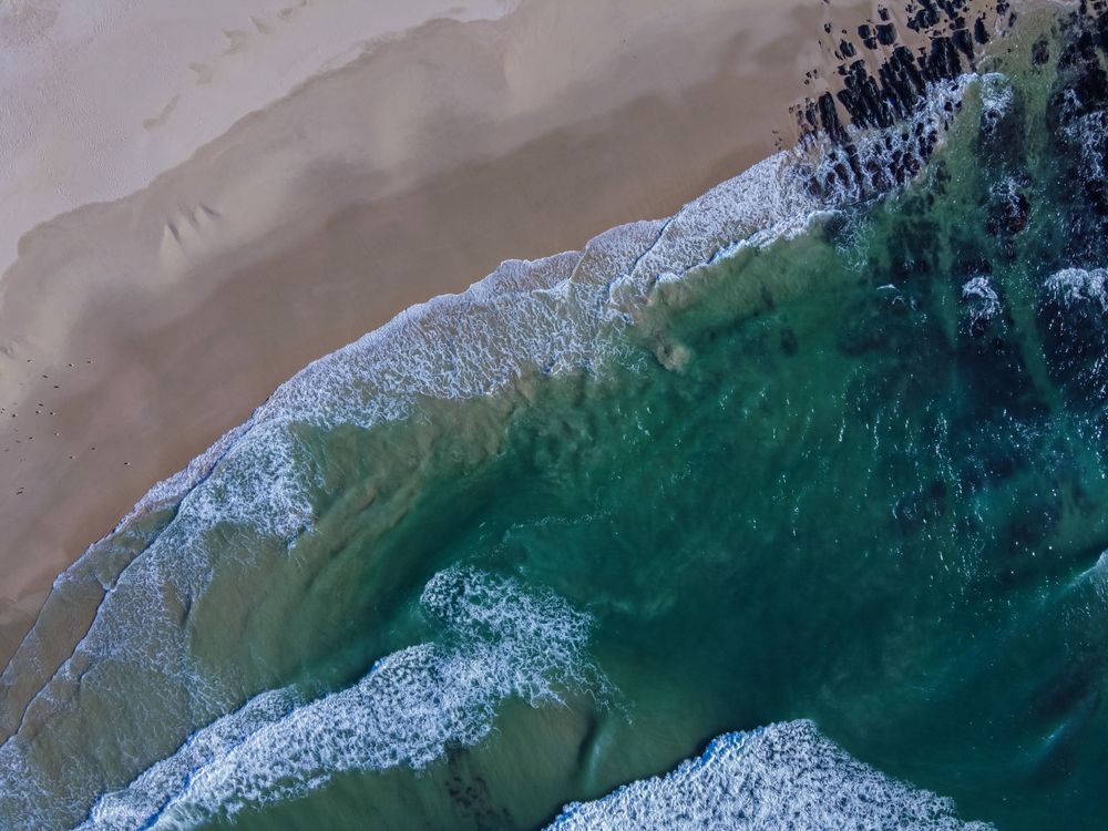 Top-down aerial view of turquoise ocean waves washing onto a sandy beach shoreline.