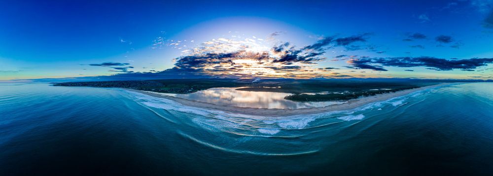 Stunning aerial panoramic sunset over calm ocean waters with dramatic cloud reflections.