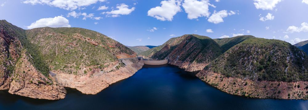 Aerial panoramic view of a deep blue reservoir surrounded by rugged mountain canyon walls.