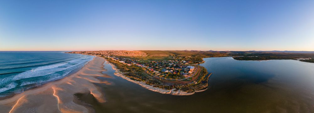 Aerial panoramic view of a coastal town at golden hour beside a calm estuary.