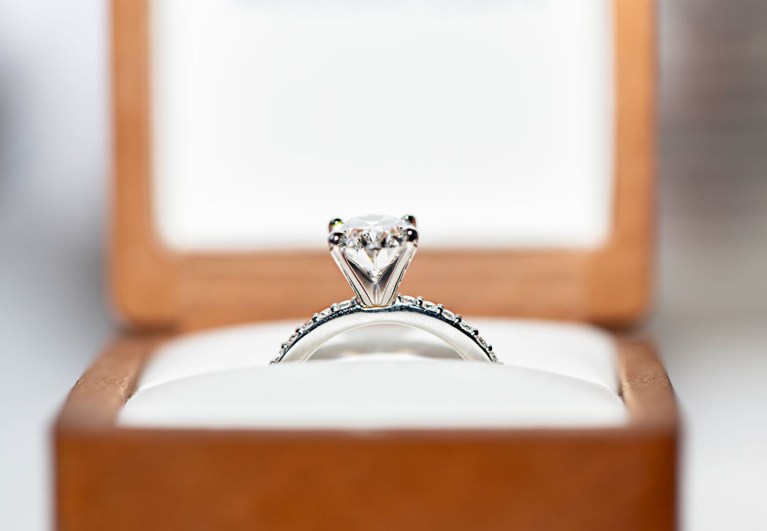 Elegant diamond engagement ring displayed in a wooden ring box with natural lighting.