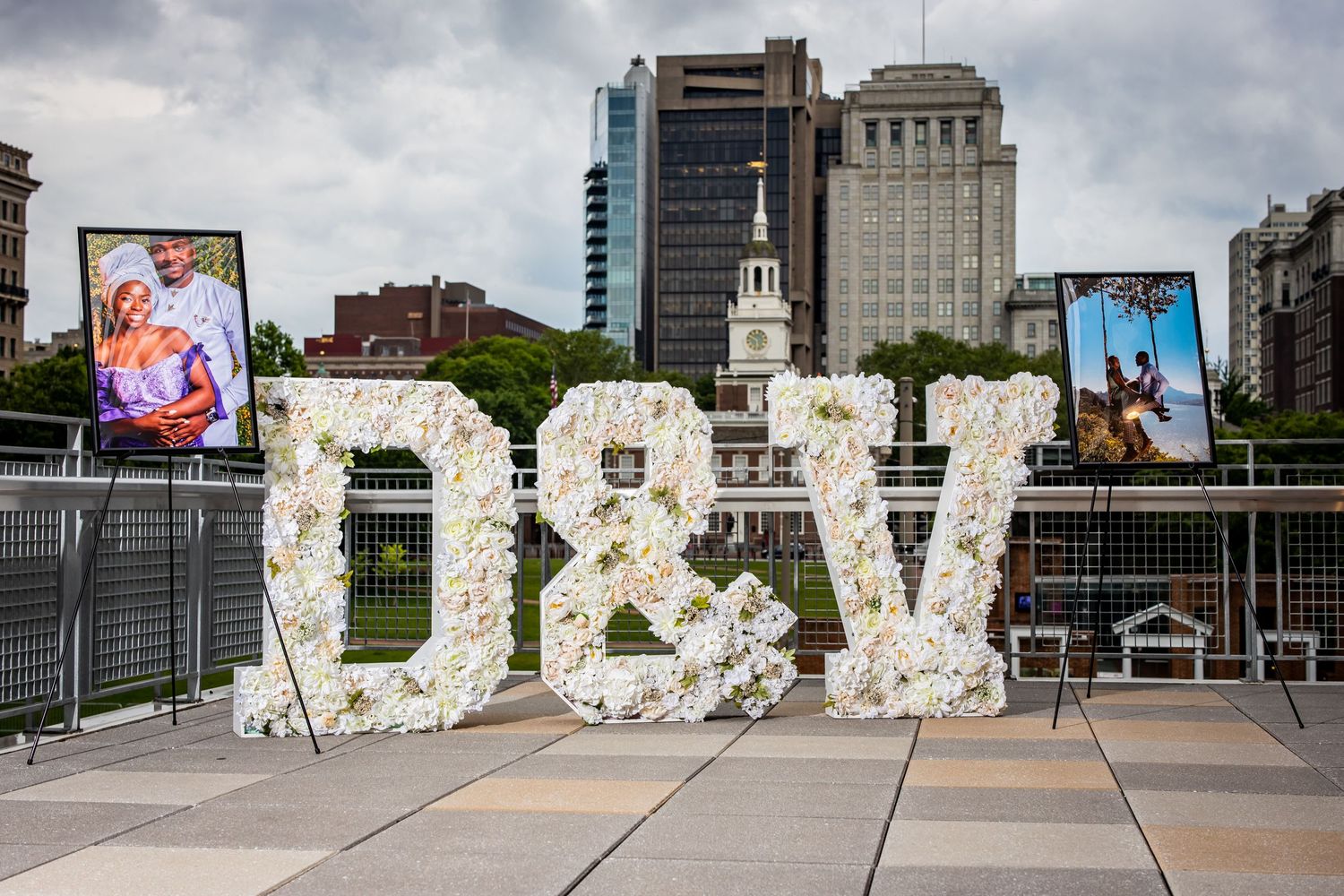 Large white D&V letters with floral decorations displayed against a city skyline background.