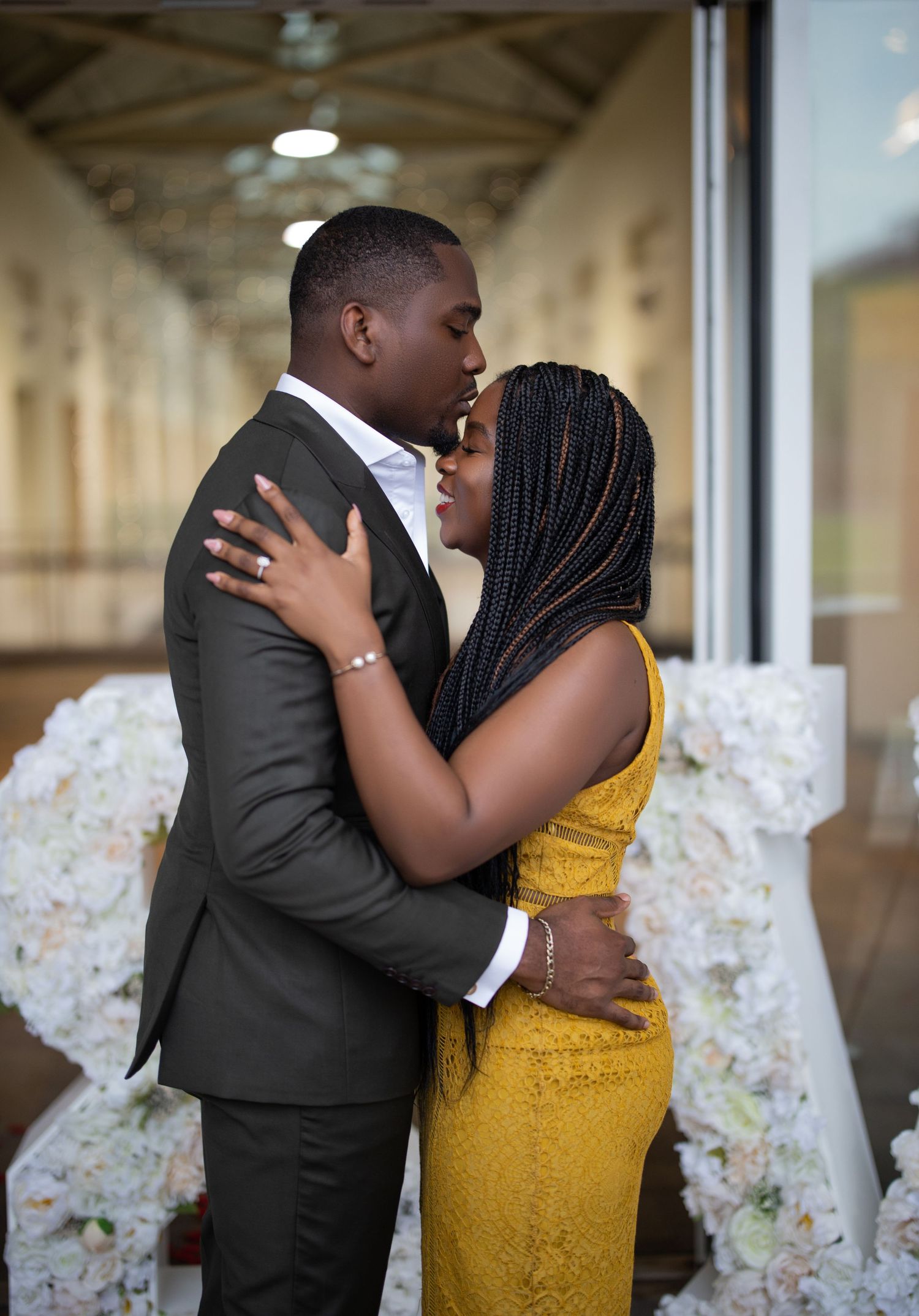 A romantic embrace between a couple wearing formal attire, with floral decor in the background.