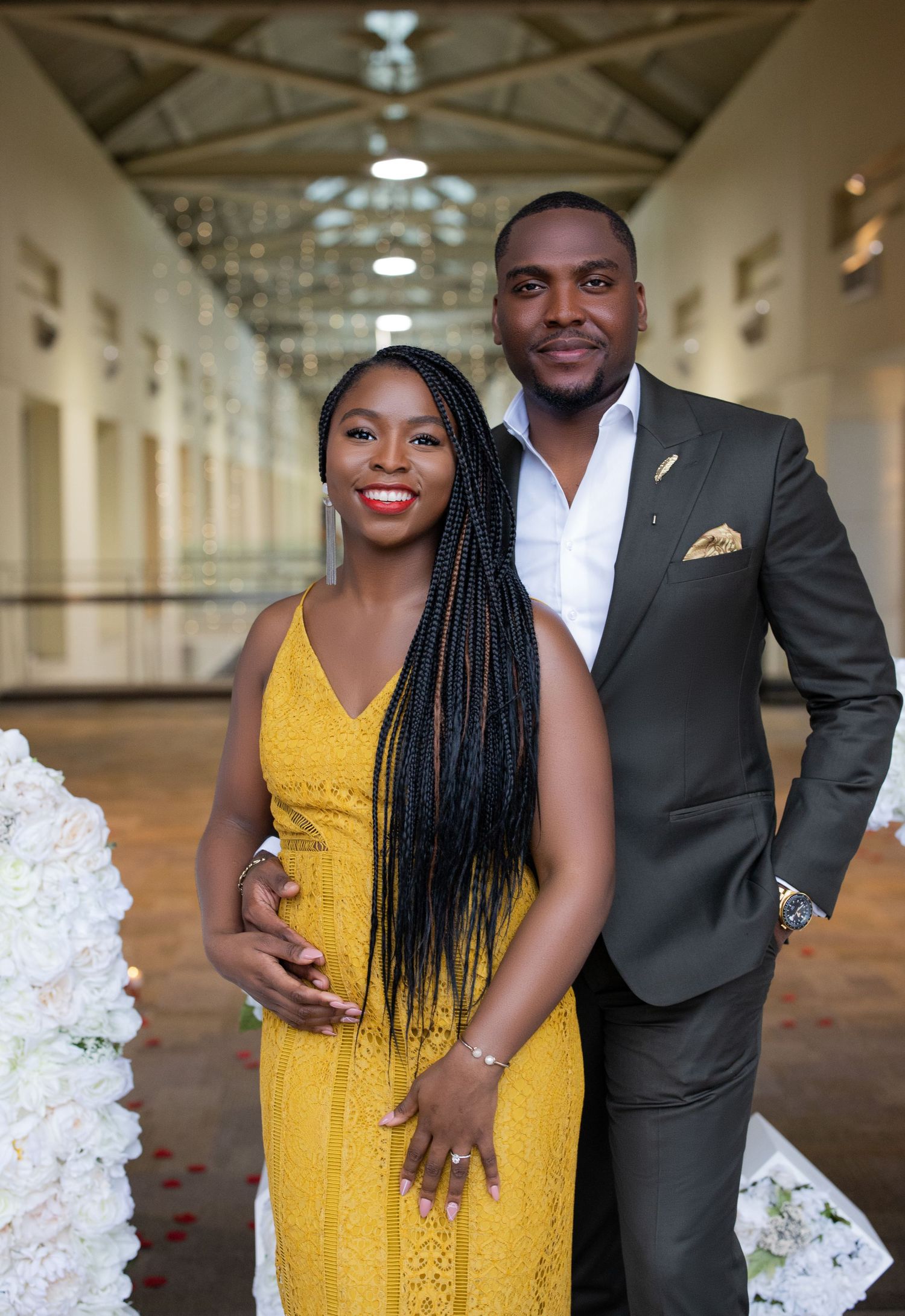 A couple in formal wear smiling at the camera in an elegant hallway setting.