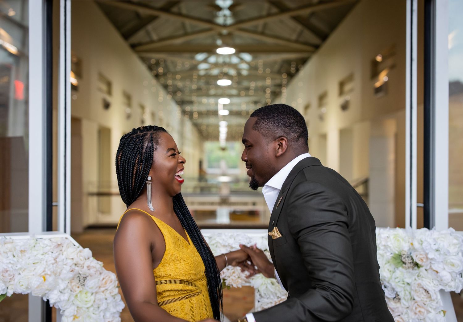 A couple sharing a laughing moment in an elegant hallway with white floral decorations.