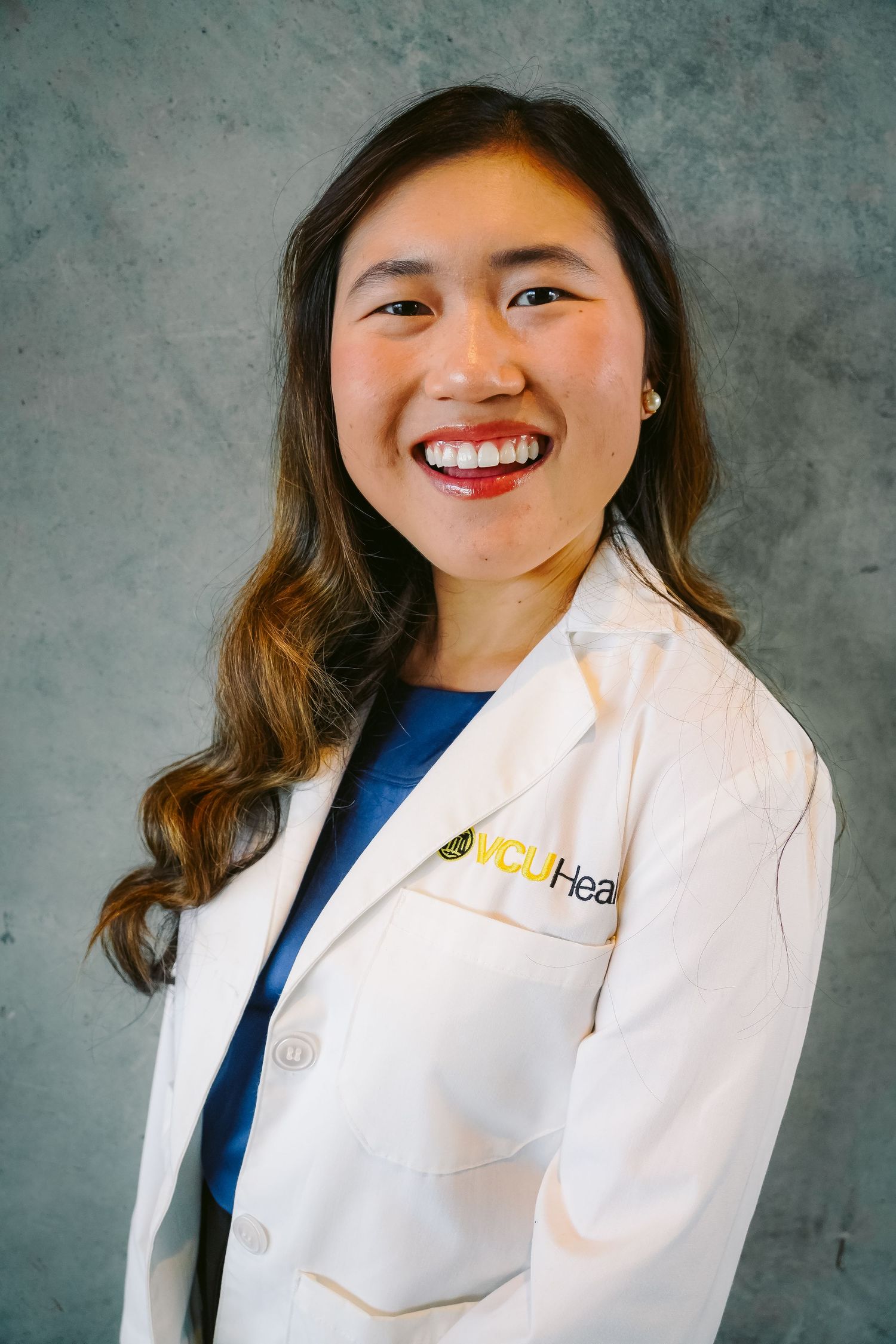 Professional portrait of healthcare worker in white coat against gray backdrop.