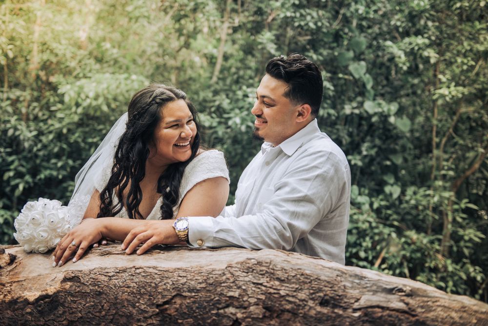 A romantic wedding photo of a couple leaning on a rock in a lush garden setting.