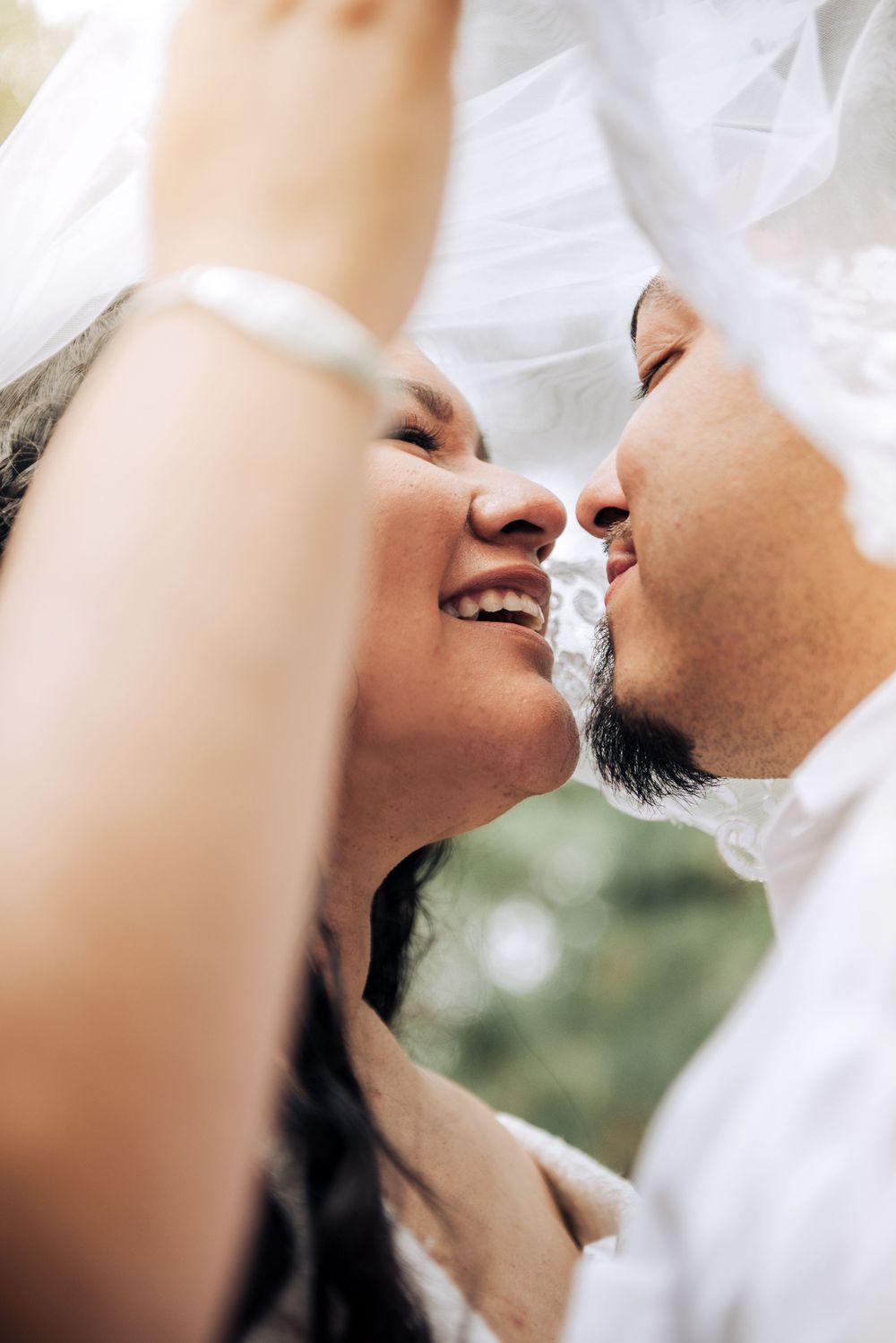 Close-up of couple sharing joyful moment under wedding veil.