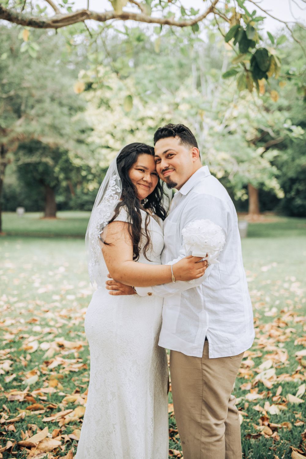 A newlywed couple embraces outdoors surrounded by fall foliage.