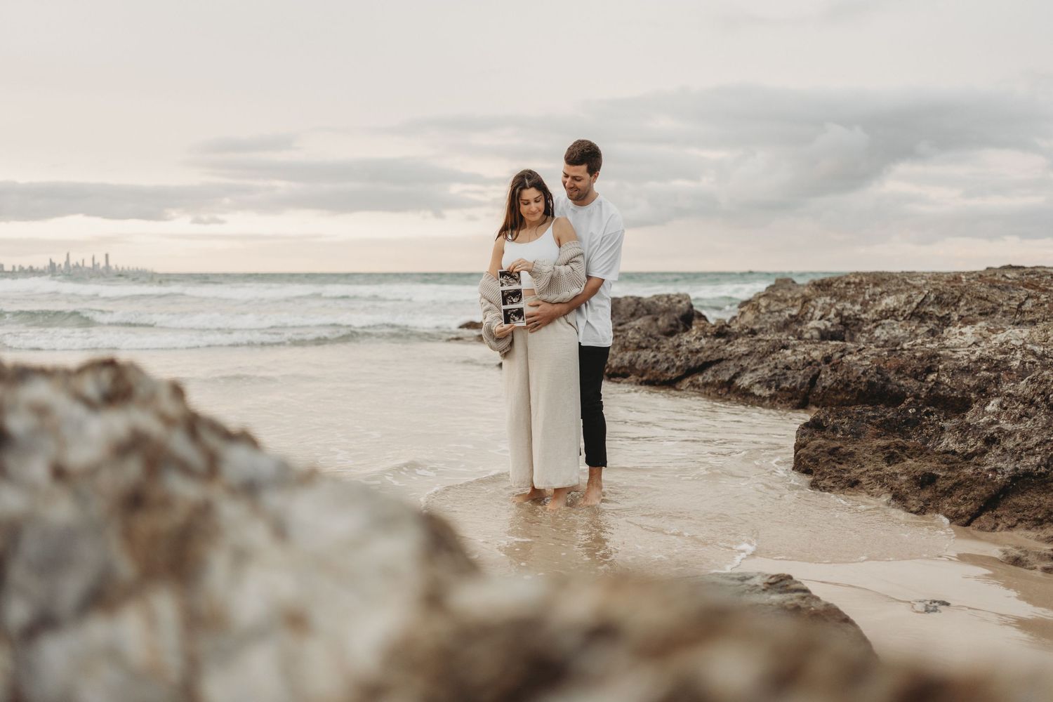 pregnancy announcement on a Gold Coast beach, featuring a couple holding an ultrasound photo capturing their excitement