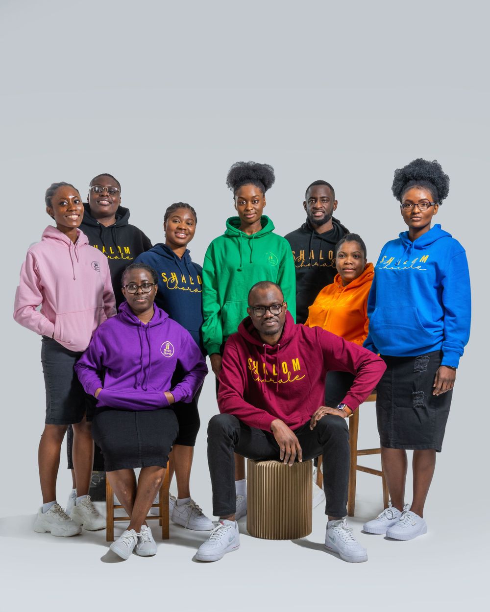 Group of nine people wearing colorful branded hoodies posing for a professional studio portrait.