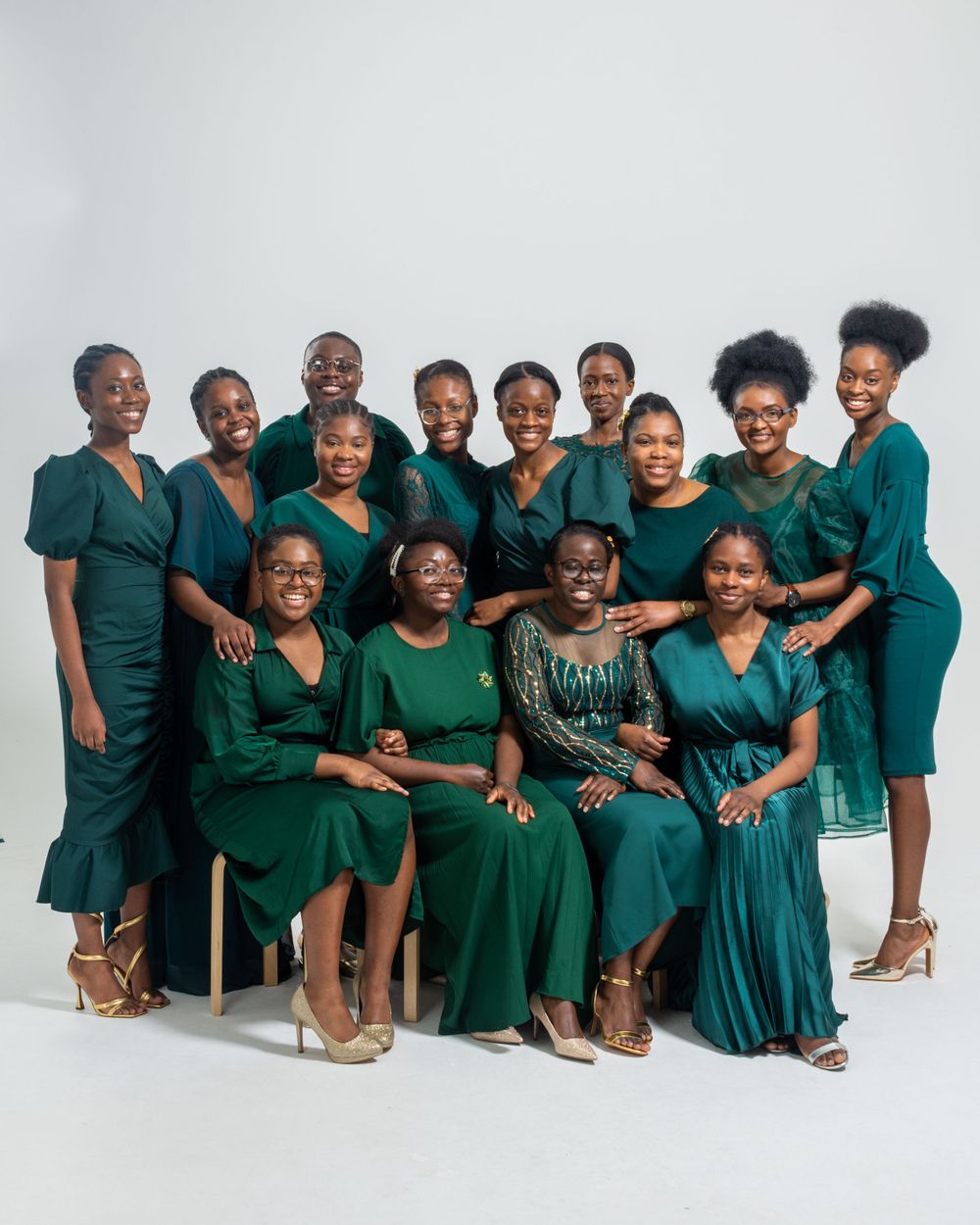 Large group of women in matching dark green dresses posing together for a professional portrait.