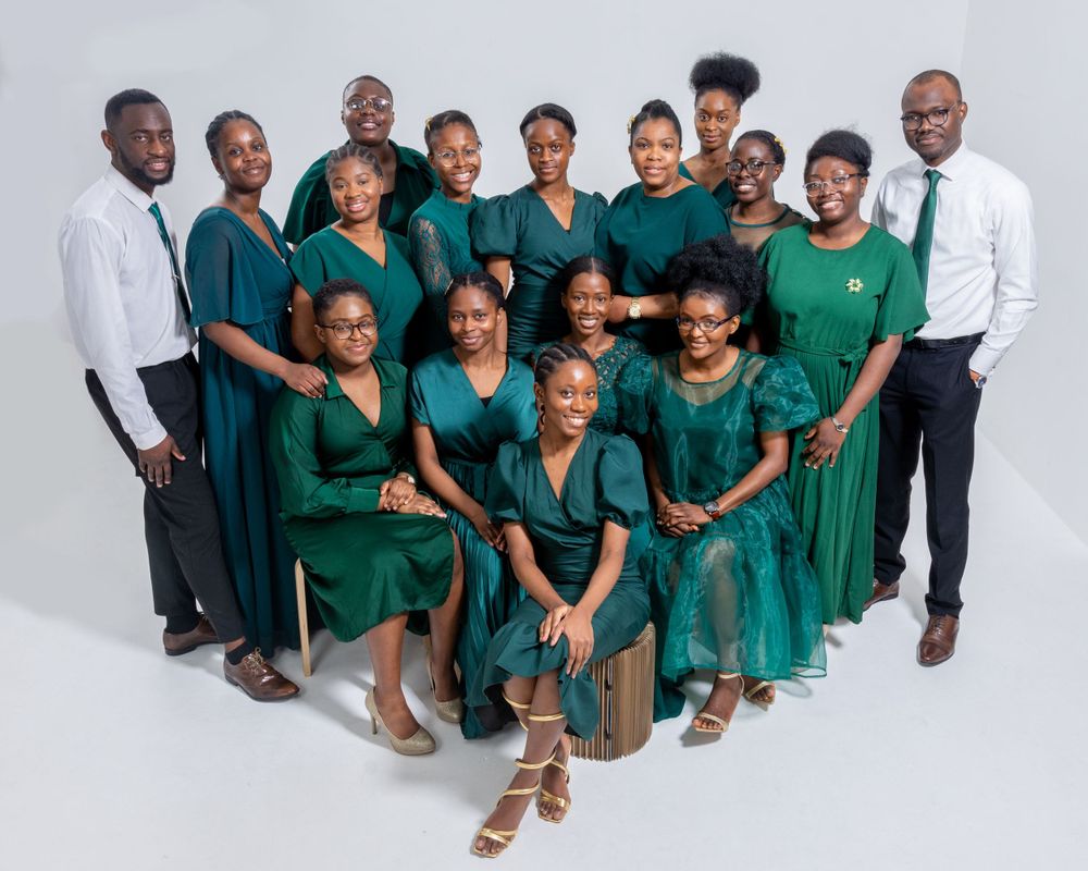 Large group in teal dresses with two men in white shirts posing for a formal group portrait.