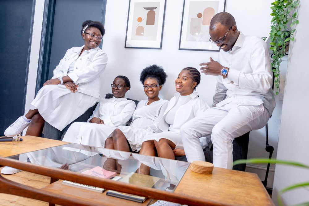 Family of five posing together in matching white outfits on a modern sofa in a bright living room.